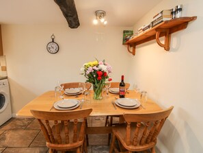 Une table à manger dressée pour quatre personnes, avec des chaises, un vase de fleurs, une bouteille de vin et une horloge au mur.