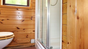 Une salle de bain aux murs lambrissés, équipée de toilettes, d’une douche à parois de verre et d’une fenêtre.