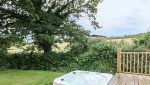 Un bain à remous sur une terrasse en bois, avec vue sur un champ verdoyant et des arbres.