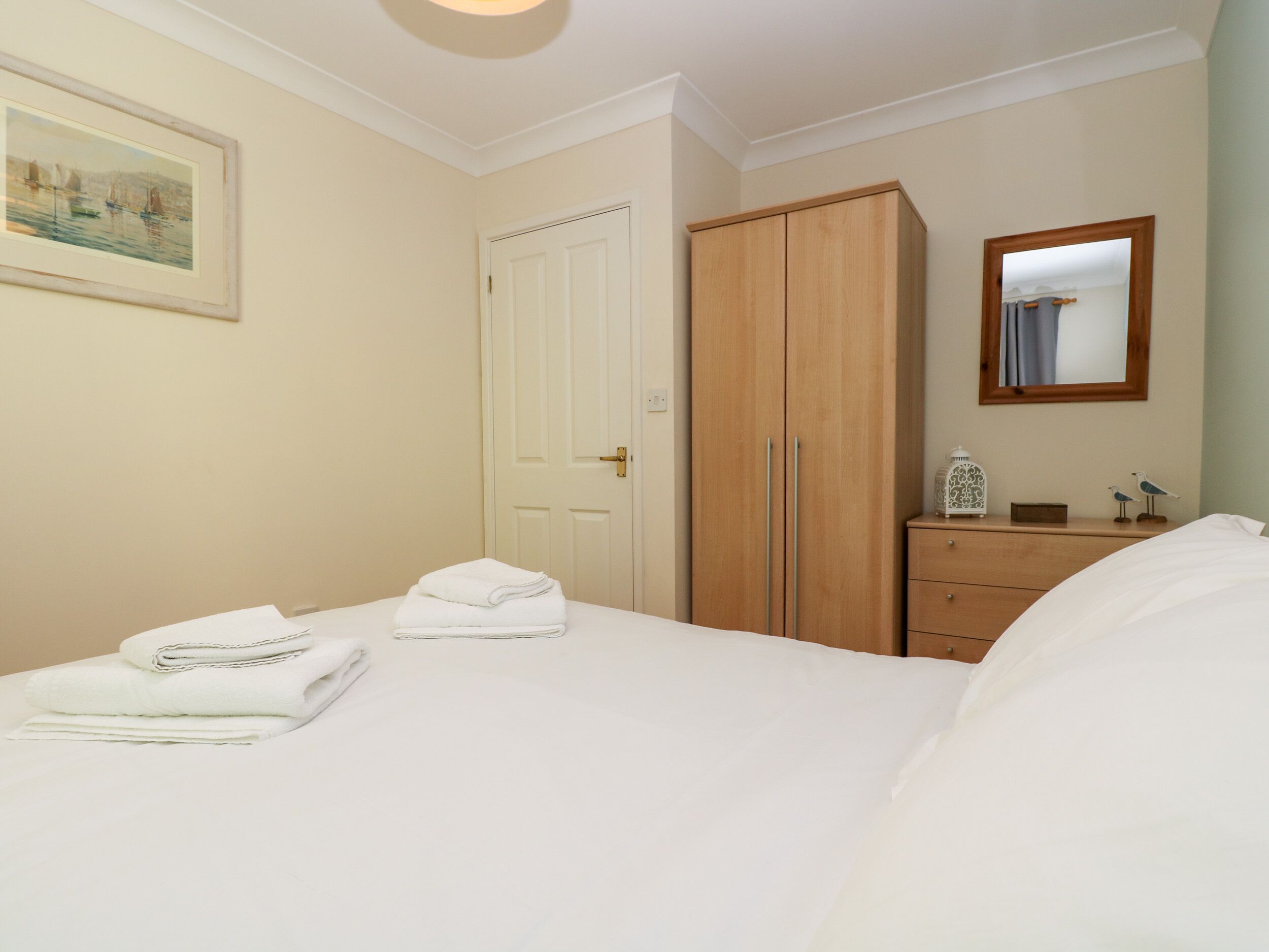 A bedroom with a bed, a wardrobe, a dresser, a mirror, and a painting on the wall.