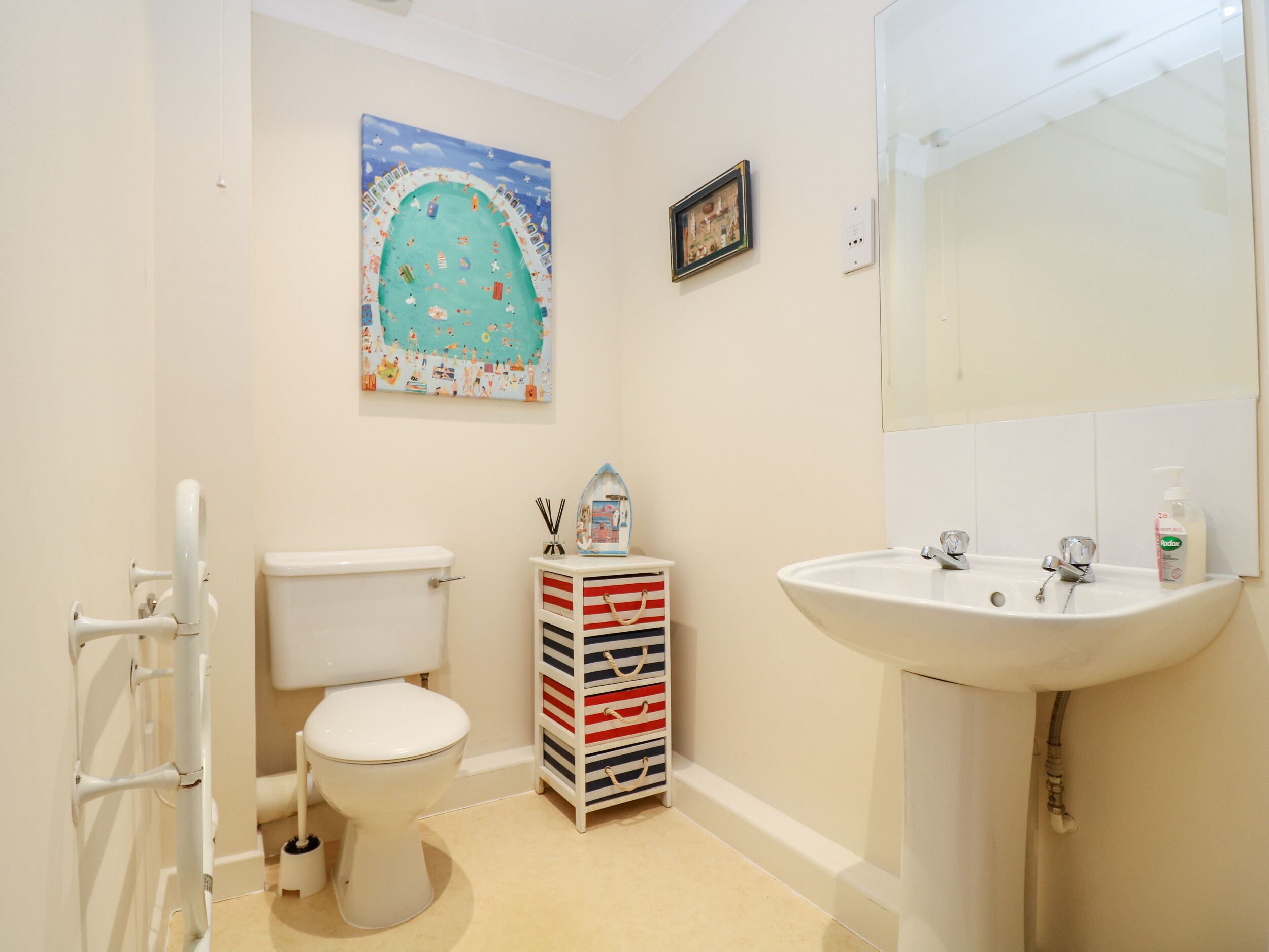A bathroom with a toilet, a sink, a mirror, a painting, and a storage unit.