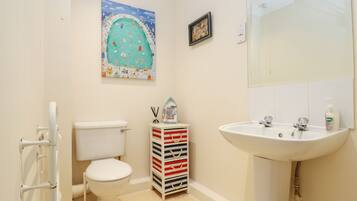 A bathroom with a toilet, a sink, a mirror, a painting, and a storage unit.