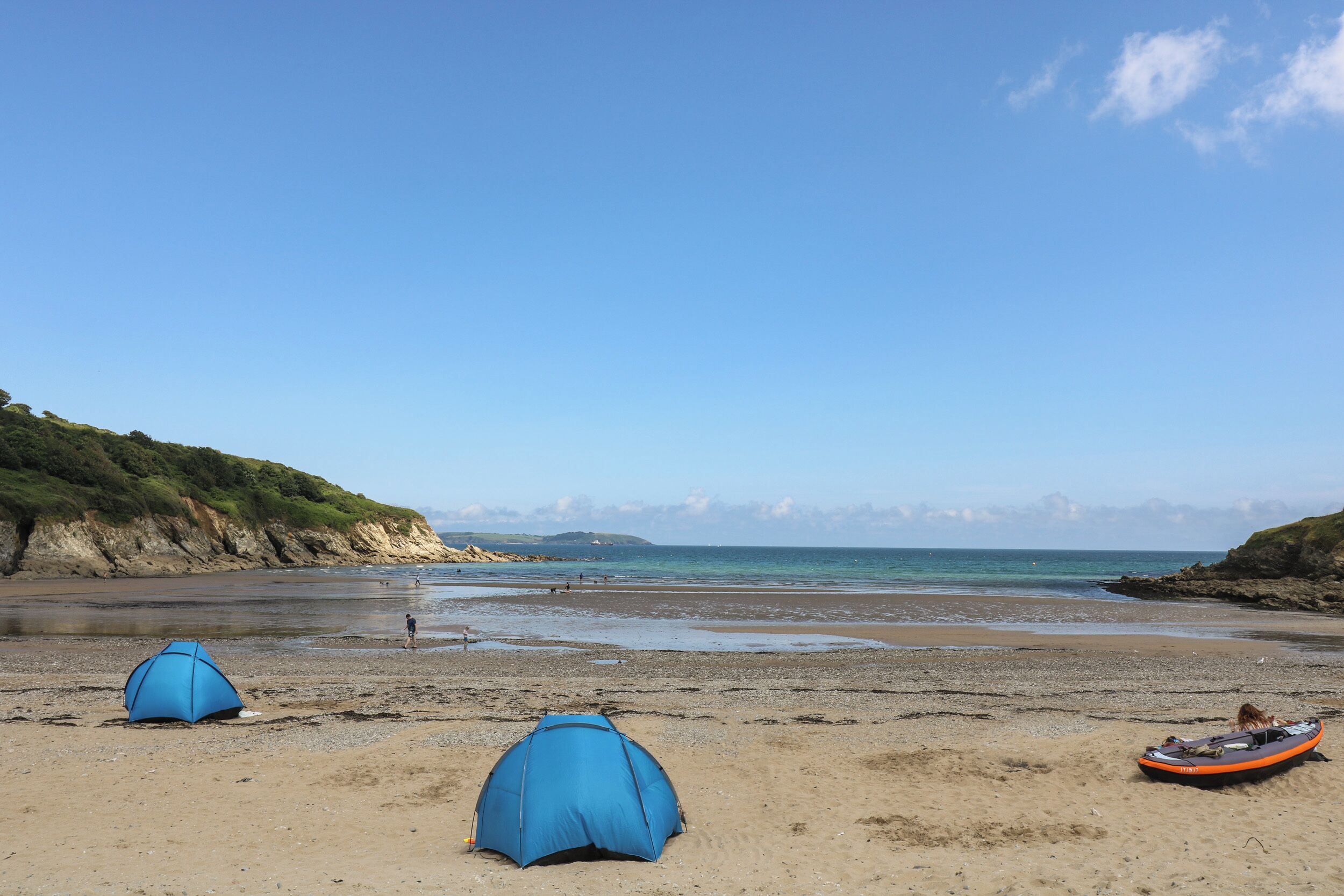 A beach with two blue tents and a boat.