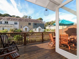 Una terraza de madera con mobiliario exterior, vistas a casas y un cielo despejado.