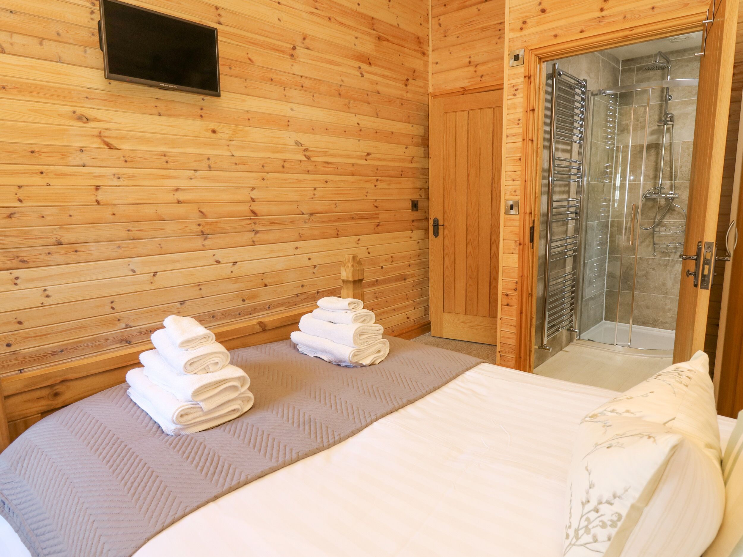 A wooden cabin room with a bed, a wooden door, and a shower area.