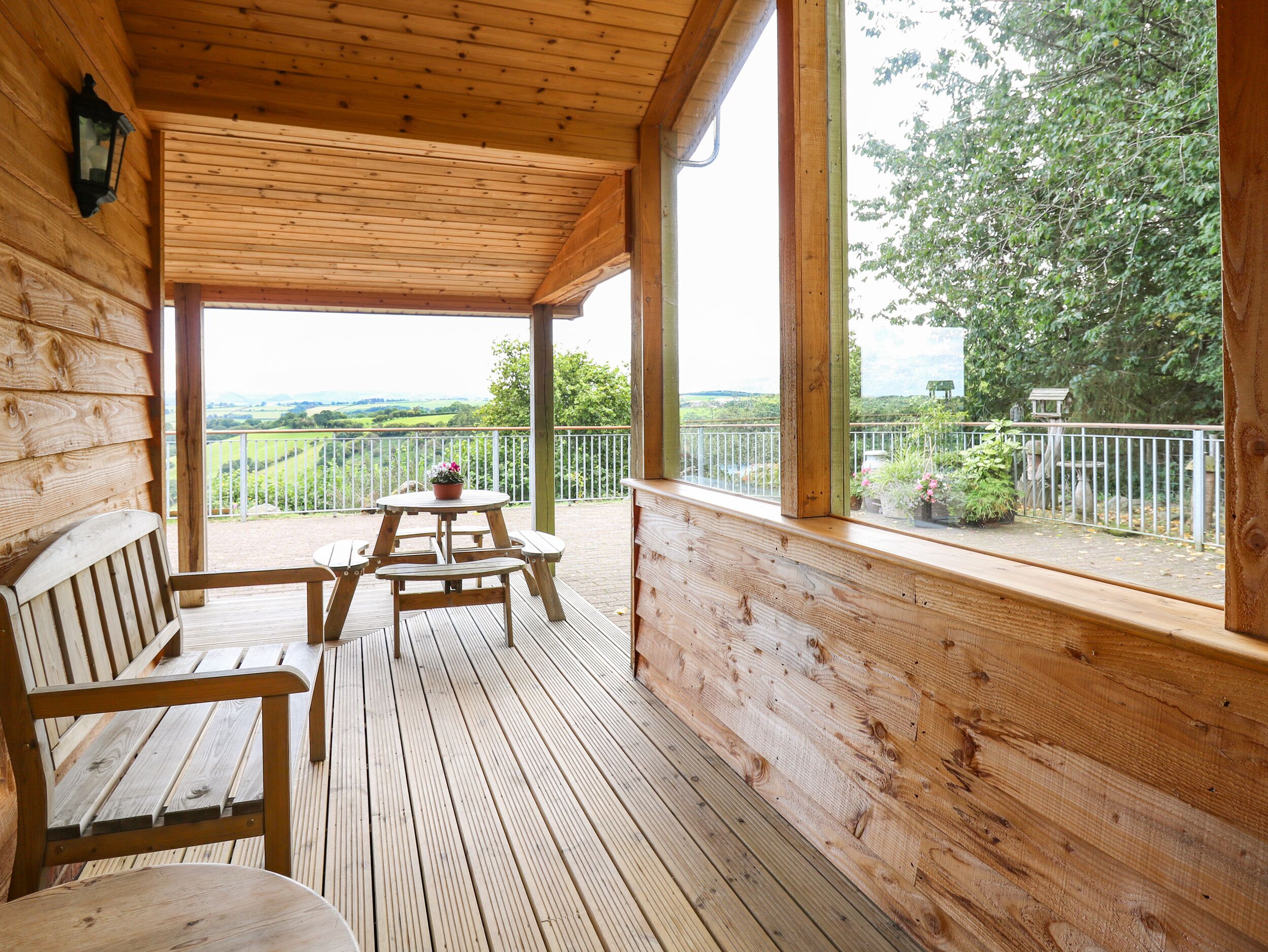 Una terraza de madera con una mesa y bancos, con vistas a un paisaje pintoresco.
