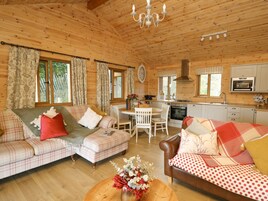 Interior acogedor de una cabaña con techo de madera, comedor, cocina y dos sofás tapizados con cuadros.