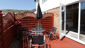 Eine Terrasse mit Tisch und Stühlen, ein roter Holzzaun und eine Glastür, die zu einem Innenraum führt.