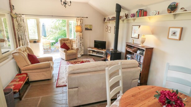 A cozy living room with a fireplace, comfortable seating, a television, and a bookshelf. - Henhouse Cottage (York)