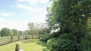 A grassy area with a wooden fence, a stone sculpture, and dense foliage. - Henhouse Cottage (York)
