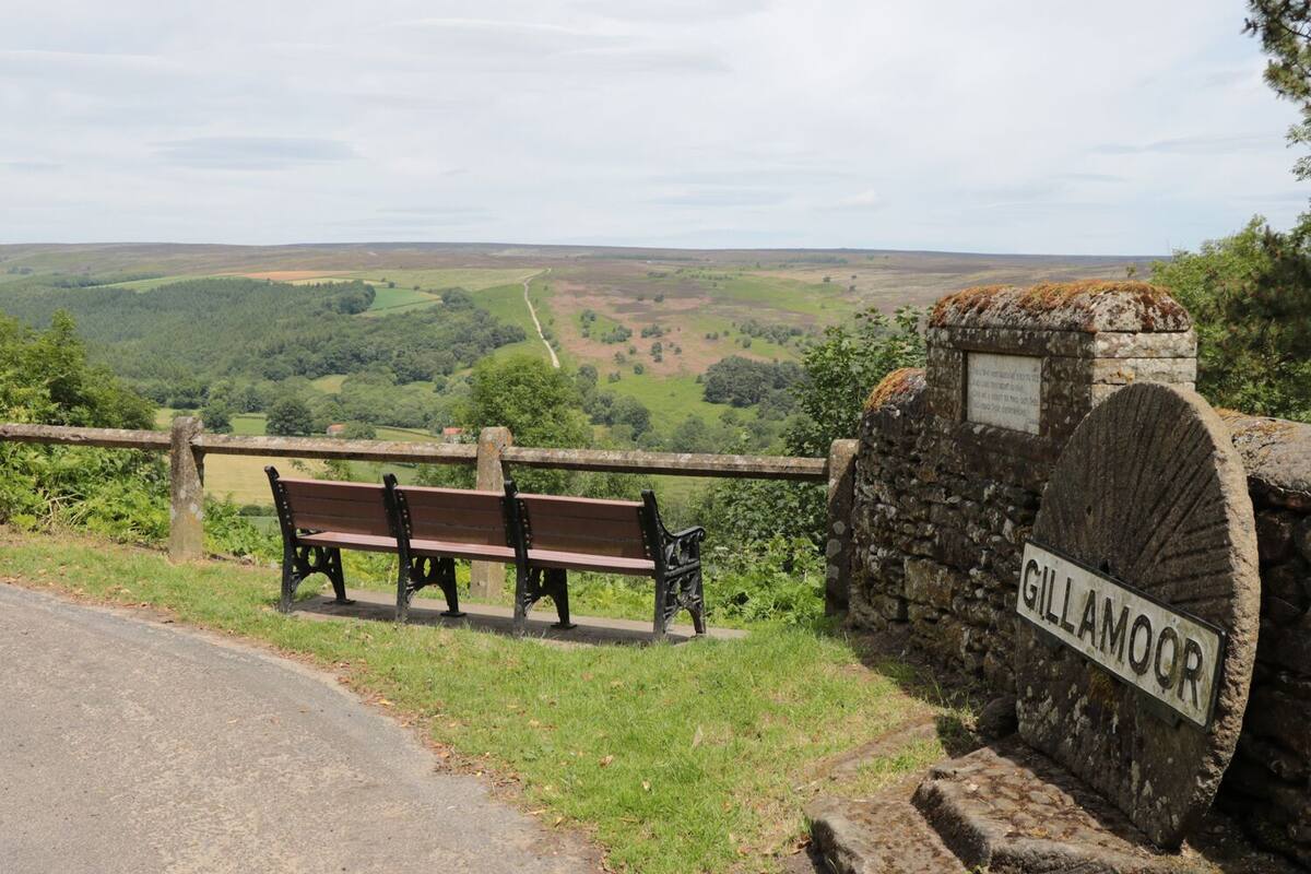 A bench and a stone sign with the name 'GILLAMOOR' in a rural setting with a view of rolling hills.