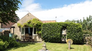 A stone house with a tiled roof, a wooden fence, and a well-maintained lawn. - Henhouse Cottage (York)