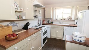 A kitchen with white cabinets, a wooden countertop, a stove, a sink, and a refrigerator. - Henhouse Cottage (York)