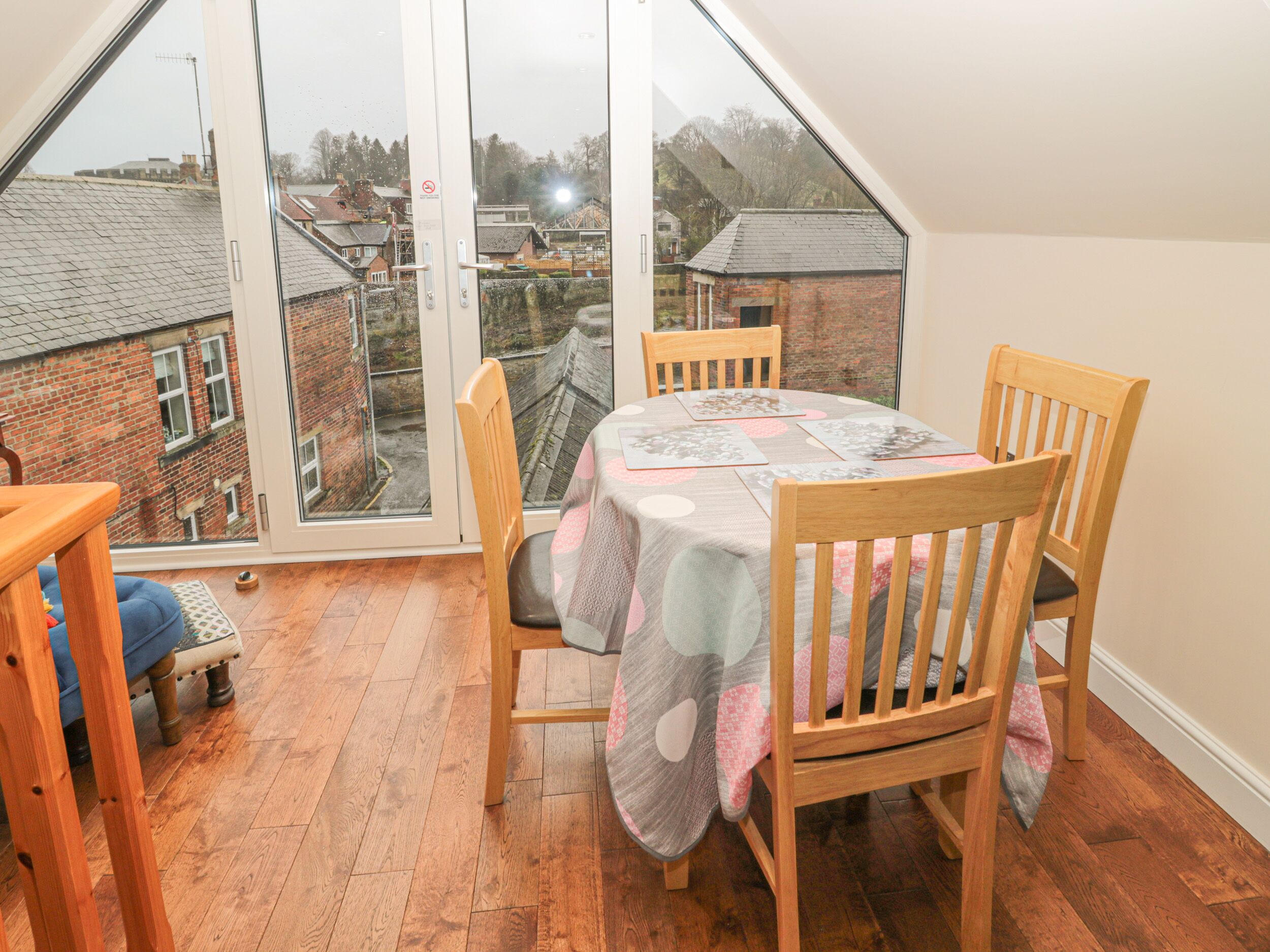 A dining area with a table and chairs, a view through a large window, and a wooden floor.