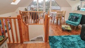 A spacious loft with a wooden staircase, a dining area with a table and chairs, and a view of the neighborhood. - River Cottage (Morpeth)
