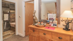 A wooden vanity with a mirror, a lamp, and a decorative deer head. There is a basket with flowers and a welcome sign for River Cottage. - River Cottage (Morpeth)