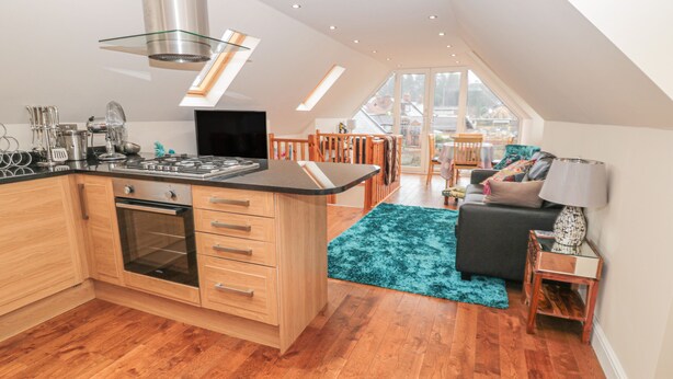 A modern kitchen with a central island, wooden cabinets, and a built-in oven. - River Cottage (Morpeth)