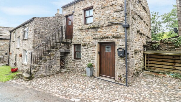 A stone building with a wooden door, a small window, and a metal staircase. - Heugh Barn (Richmond)