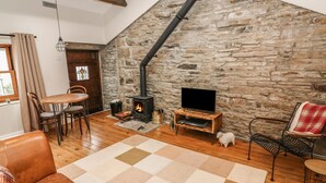 A cozy living room with a stone wall, a fireplace, a television on a wooden stand, and leather furniture. - Heugh Barn (Richmond)