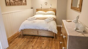 A bedroom with a wooden bed, white bedding, a wall-mounted heart-shaped light, a wooden dresser with a mirror, and a rabbit sculpture. - Heugh Barn (Richmond)