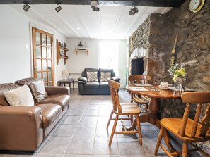 A cozy living room with a leather sofa, wooden chairs, a dining table with chairs, a fireplace, and a stone wall. - Gwenallt (Bodorgan)
