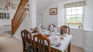 A dining room with a wooden staircase, a table set for four, and a window with a view of the countryside. - Seaview-barsloisnach Cottage (Lochgilphead)