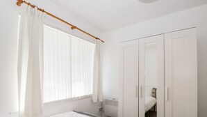 A bedroom with a bed, a wardrobe, a radiator, and a window with curtains. - Ocean Breeze (Burnham-on-Sea)
