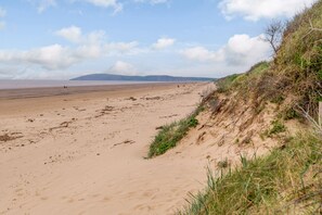 A wide sandy beach with sparse vegetation and a distant hill.