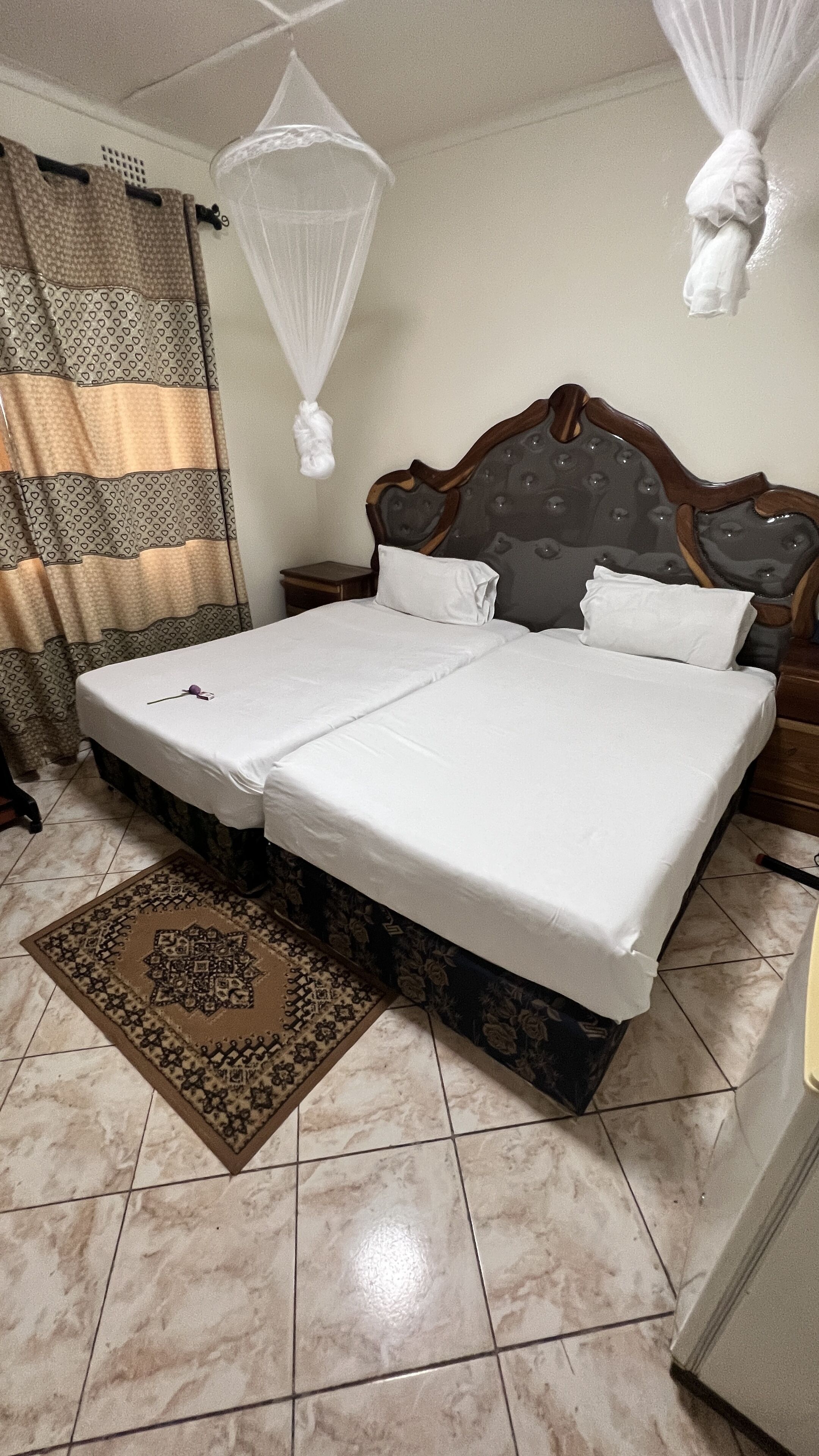 Una cama doble con ropa de cama bien tendida, un tablero de cabecera de madera, una alfombra estampada y una mosquitera colgada.