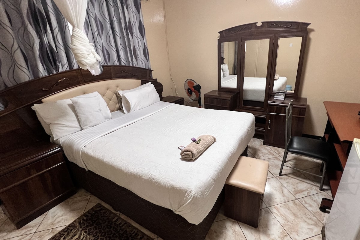 A neatly arranged bedroom with a bed, bedside tables, a dresser, a mirror, and a desk.