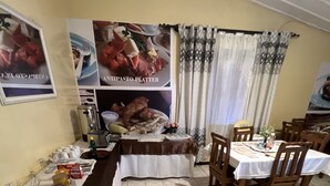 A dining area with a long counter, chairs, and a table set for a meal. - Nalikwanda Guest House (Kabwe)
