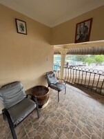 Una habitación con dos sillones grises acolchados, un taburete tejido y suelo de baldosas.