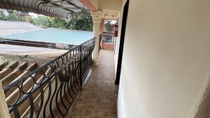 A corridor with a tiled floor, a metal railing, and a view of a building with a corrugated metal roof. - Nalikwanda Guest House (Kabwe)
