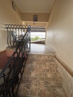 Una escalera con escalones de piedra y barandilla de metal, que conduce a un balcón con vistas a la vegetación.