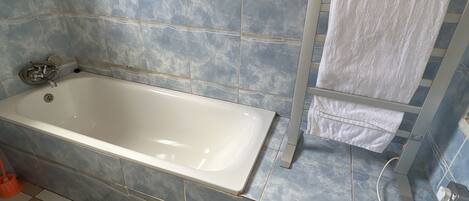 Un baño con bañera, baldosas azules y beige, una toalla blanca y un enchufe.