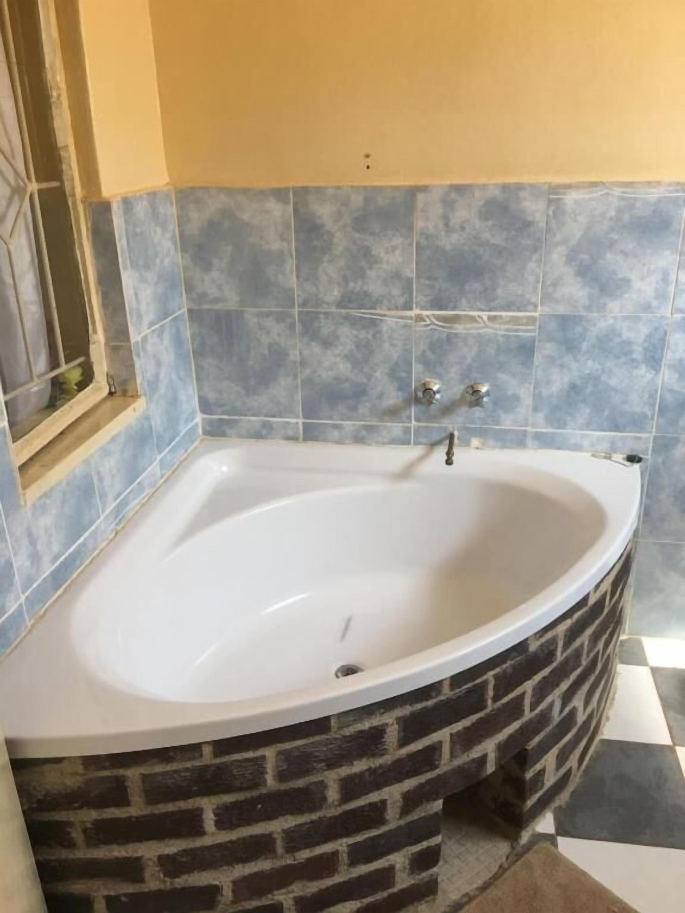 A bathroom with a freestanding bathtub, blue-tiled walls, and a brick accent wall.