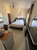 Habitación de hotel con una cama grande, un escritorio con hervidor y taza, una silla y una mesita de noche.