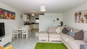A modern living room with a sofa, a dining table with chairs, a TV, and a kitchen in the background.