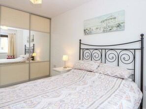 A bedroom with a bed, a nightstand, a lamp, a mirror, and a painting on the wall.