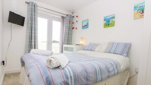 A bedroom with a bed, a TV mounted on the wall, and a window with curtains.