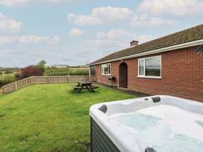 A backyard with a hot tub, picnic table, and a brick house with a view of the countryside. - Glanyrafon Bungalow (Rhayader)