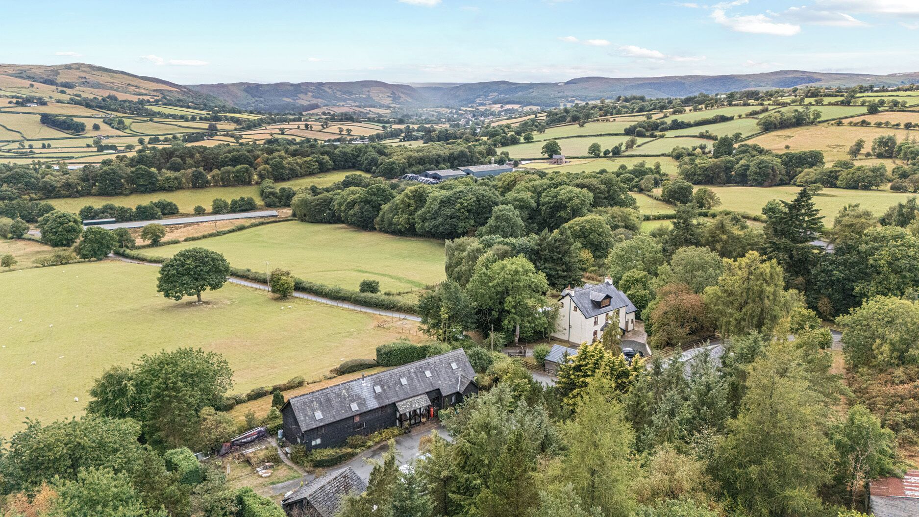 Paisagem rural com colinas ondulantes, árvores dispersas e alguns edifícios.
