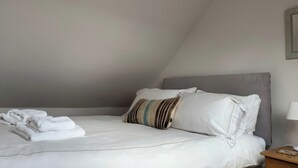 A neatly made bed with white linens, a grey headboard, and a striped pillow. - Solas (Sleat)