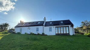 A white house with a black roof, a garage door, and a small garden. - Solas (Sleat)
