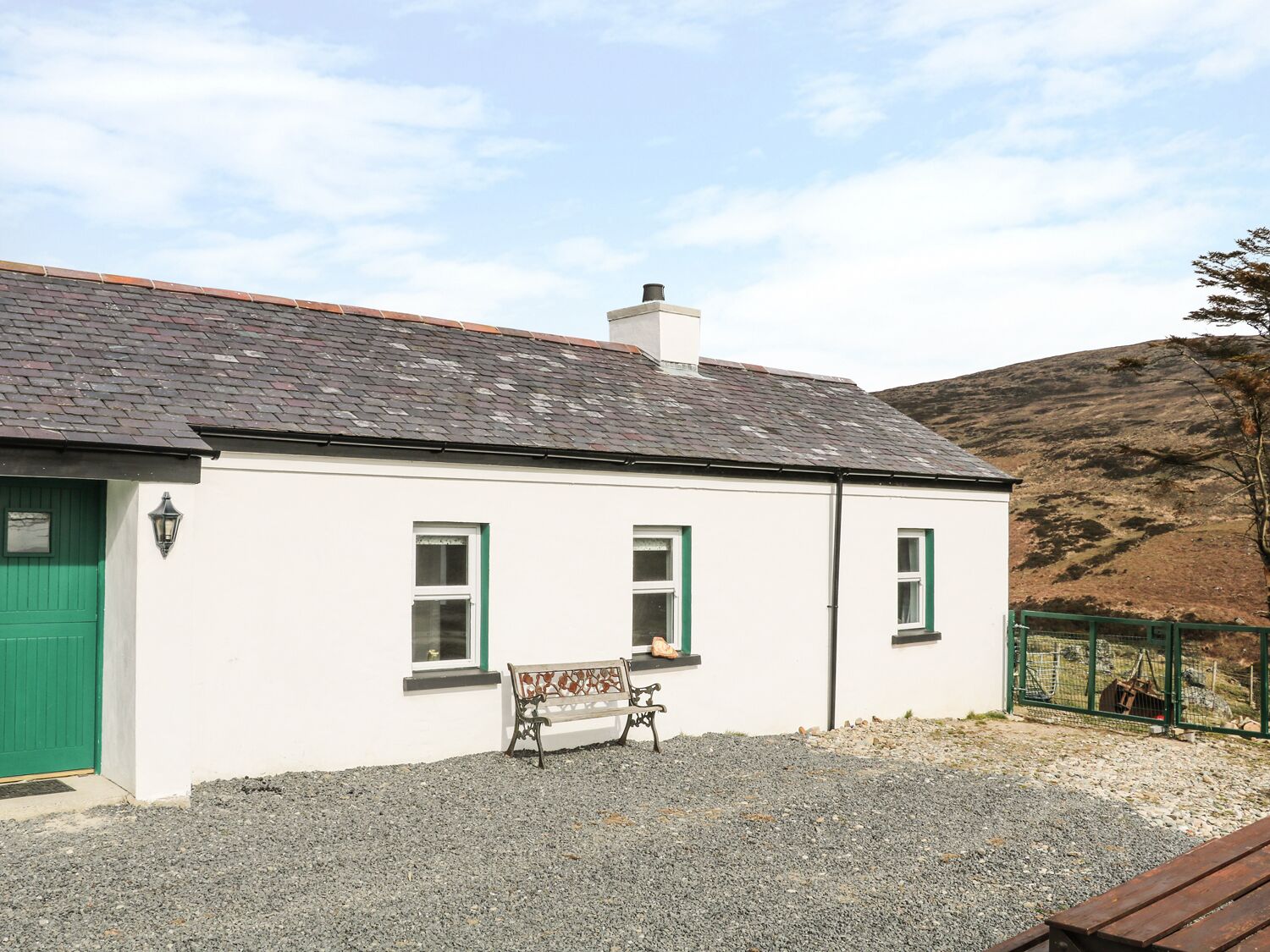 A white building with a grey roof, a green door, and a bench in front.
