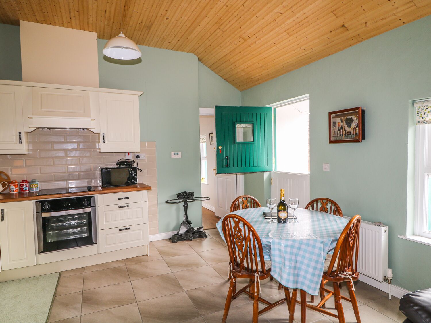 A kitchen with white cabinets, a microwave, and an oven. There is a table with a checkered tablecloth and two chairs.
