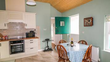 A kitchen with white cabinets, a microwave, and an oven. There is a table with a checkered tablecloth and two chairs.