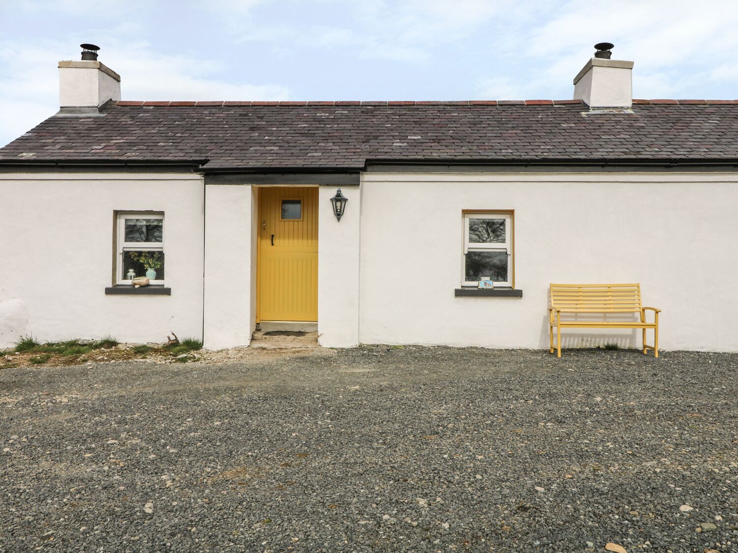 A single-story house with a yellow front door, two chimneys, and a gravel driveway.