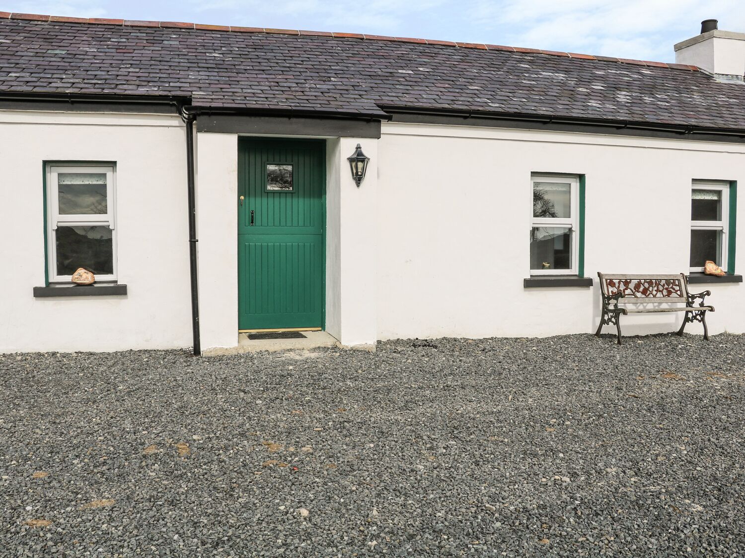 A white building with a green door, two windows, and a bench.