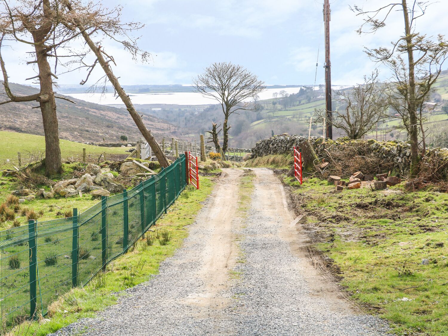 A gravel path leading to a stone wall with a view of a lake and hills.